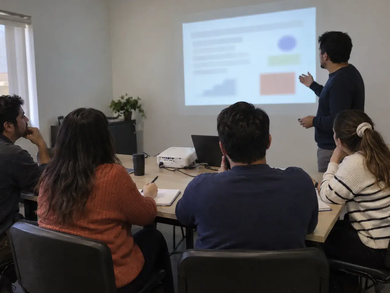 Personas en una sala de reuniones mirando una proyección mientras alguien explica